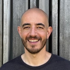 Re:Axis, smiling, in front of a weathered wooden wall.